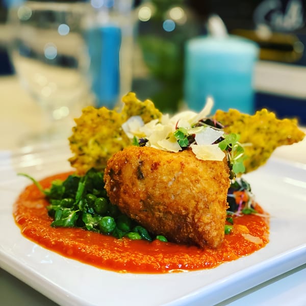 Crispy fried chicken with green peas, red sauce, and parmesan on a white plate.