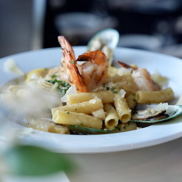 Close-up of rigatoni pasta with shrimp, mussels, and parmesan cheese on a white plate.