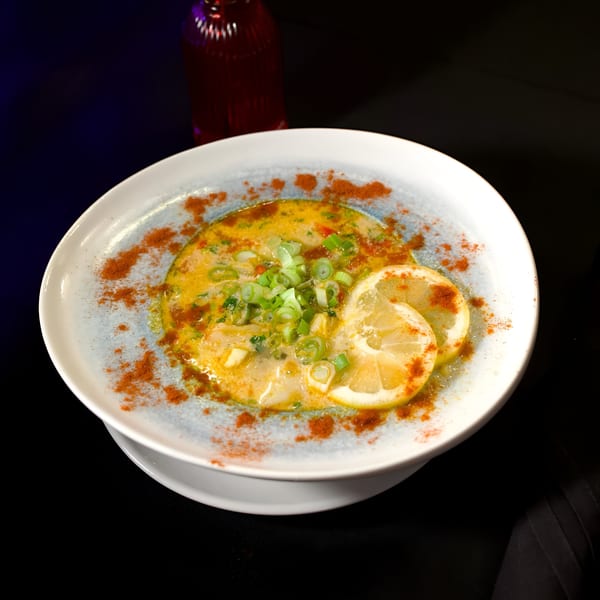 Mediterranean seafood dish with lemon slices, green onions, and paprika in a white bowl.