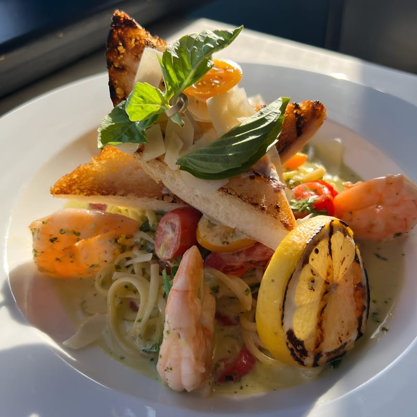 Shrimp pasta with grilled bread, basil, cherry tomatoes, and a grilled lemon wedge.